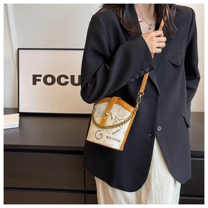 Detail of cream canvas bucket bag with brown leather trim and golden chain on model