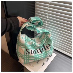 Detail of green and white checkered canvas shoulder bag with simple typography and wide strap