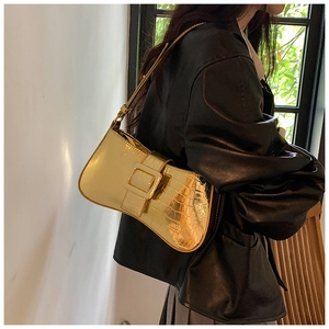 Detail of gold metallic underarm bag featuring crocodile pattern and square buckle