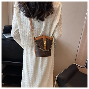 Close-up of brown bucket bag with monogram print and golden chain strap detail