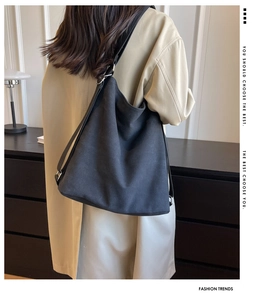 Rear view of model wearing a black canvas shoulder bag with adjustable wide strap