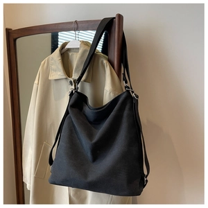 Detail of black canvas tote bag showing wide shoulder strap and silver metal buckle