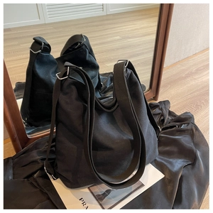 Detail of black canvas tote bag showing wide shoulder strap and silver metal buckle