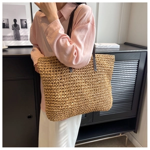 Detail of straw woven tote bag with brown leather shoulder straps shown on a model