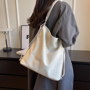 Minimalist beige large capacity canvas tote bag worn as a shoulder bag for daily commuting