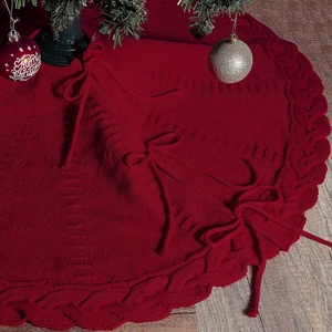 Falda roja de punto para árbol de Navidad con trenzado y lazos sobre suelo de madera