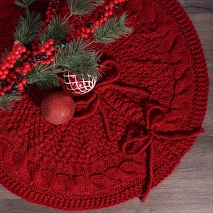Close-up of red cable knit Christmas tree skirt with bow tie on wooden floor