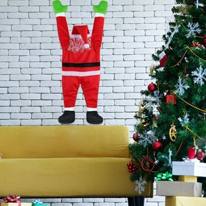 Hanging climbing Santa Claus decoration with green gloves on a white brick wall