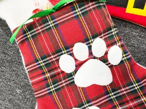 Macro detail of Christmas bone sock featuring plaid pattern and white plush paw print