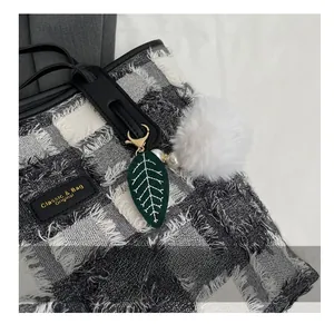 Detail of tweed tote bag with embroidery leaf pendant and white faux fur ball charm