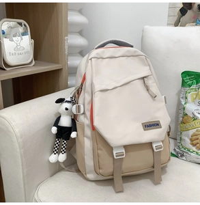 Détail d'un sac à dos beige avec poches contrastées, boucles et breloque chien peluche