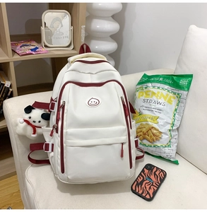 Close-up of contrast zipper detail and plush puppy charm on minimalist white backpack