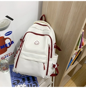 Detail of white nylon backpack with red straps and drop-shaped smiley logo on a desk