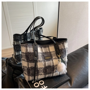 Detail of checkered canvas tote bag with black leather straps and soft fur ball charm