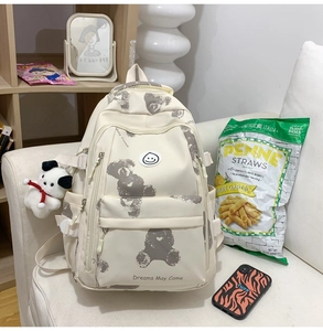 Close-up of beige school backpack featuring bear print and plush puppy accessory