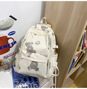 Detail of off-white backpack with gray bear patterns and side pockets by a bookshelf
