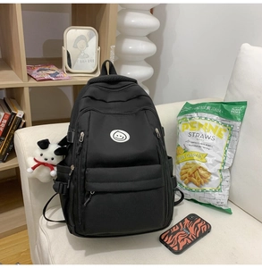 Detail of a black nylon backpack with a smile logo and a plush puppy keychain on a sofa