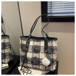 Detailed view of black and white checkered tote bag with fringe trim and plush charm