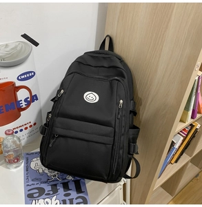 Detailed view of black large capacity nylon backpack with smiley face logo by a bookshelf
