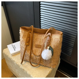 Detail of canvas tote bag featuring textured fringe grid and decorative white pom pom charm