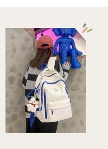 Detail of a large cream and blue backpack with a plush puppy charm and a smiley face logo