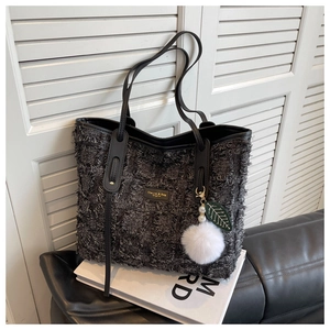 Detail of grey tweed tote bag featuring black leather handles and a white fur ball charm