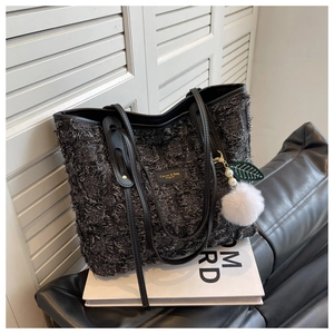 Close-up of black canvas tote bag with leather straps and plush charm on leather sofa