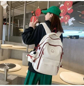 Detail view of large white backpack with red trim and cute panda plush charm on model