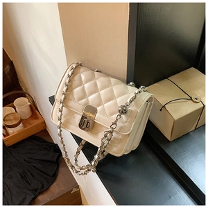 Close-up of cream quilted crossbody bag with silver twist lock and chain strap detail