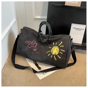 Detail of black canvas travel bag featuring colorful graffiti prints and leather handles