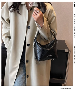 Close-up of black quilted shoulder bag with metal JINGPIN logo on khaki trench coat
