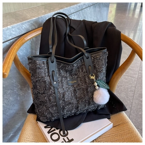 Close-up of tweed tote bag with fringe detail and luxury plush charm on a chair
