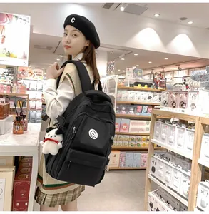 Detail of large black nylon backpack featuring a white smiley badge and puppy plush charm