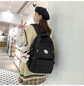 Close-up of black waterproof backpack featuring smiley badge and white plush dog pendant