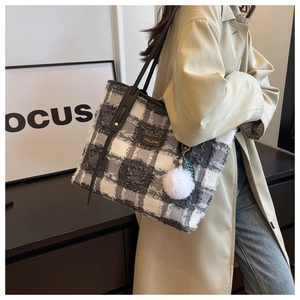 Detail view of large plaid canvas tote bag with fringe edges and plush ball accessory
