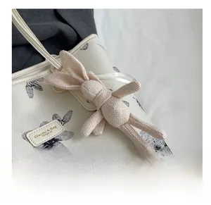 Détail d'un charm lapin en tricot beige avec ruban sur un sac fourre-tout à fleurs