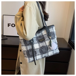 Detail of tweed checkered tote bag with fringe edges and plush pompom charm