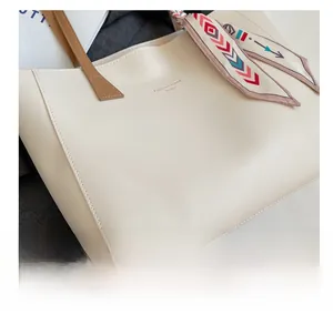 Detail of minimalist cream tote bag with brown handle and decorative silk scarf accessory