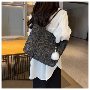 Close-up of a grey tweed tote bag with black leather straps and a white fuzzy charm