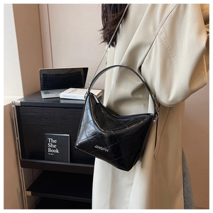 Close-up of a black quilted chain bucket bag held by a model wearing a beige trench coat
