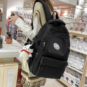Black high-capacity nylon backpack with a smiley face patch and plush puppy charm decor