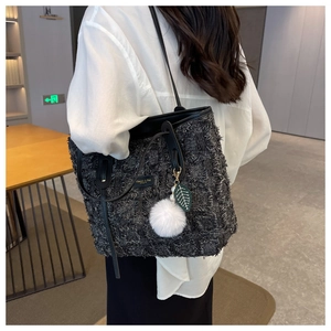 Detail of grey tweed tote bag with black leather straps and plush ball charm decoration