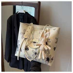 Detail of canvas tote bag featuring black floral print and cute beige knit bunny pendant