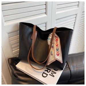 Detail of a black tote bag with brown straps, silk scarf accent, and gold lettering