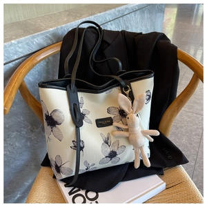 Détail du sac cabas en toile crème avec imprimé floral et anses en cuir sur chaise