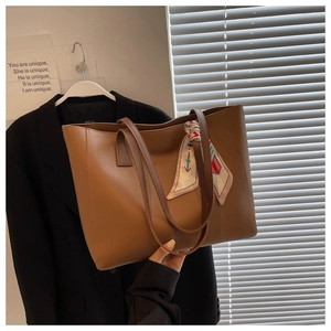 Detail of a brown leather tote bag with a colorful printed scarf on the handle