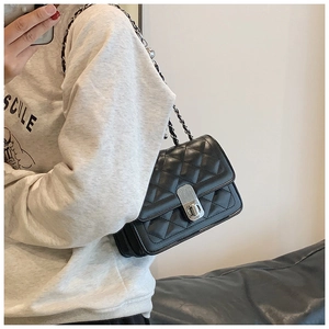 Detail of black quilted crossbody bag featuring silver chain strap and metal turn-lock closure
