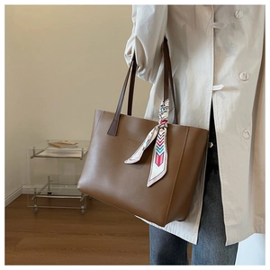 Brown large capacity tote bag with scarf handle detail worn with a trench coat