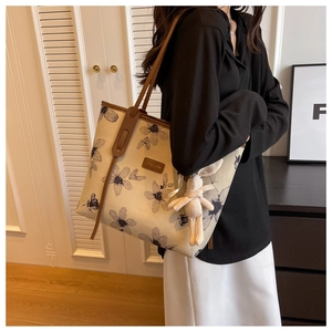 Detail of floral canvas tote bag with brown leather straps and plush rabbit charm
