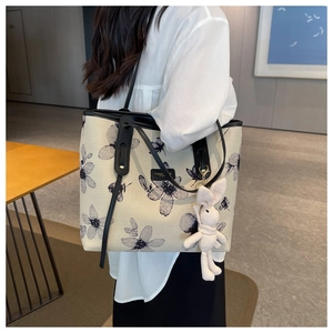 Detail of canvas tote bag with floral print, leather straps, and plush bunny charm